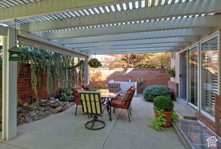 Patio with a slatted pergola, concrete flooring, and a brick privacy wall