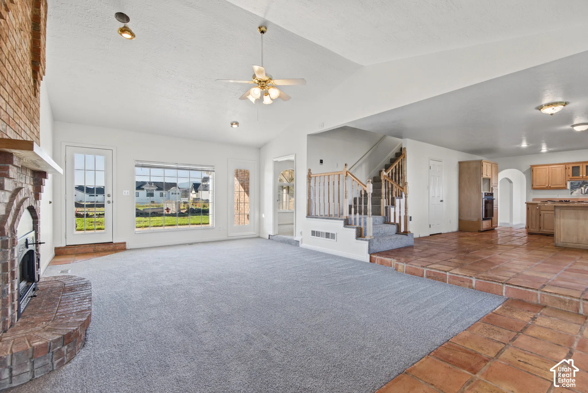 Vaulted ceilings, brick fireplace with a raised hearth, terracotta tile flooring, staircase with a wood railing, and built-in cabinetry