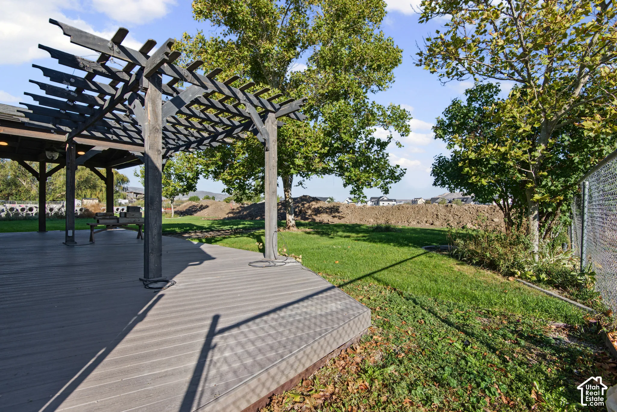 Backyard featuring a wood deck, structural pergola, manicured lawn, and mature trees