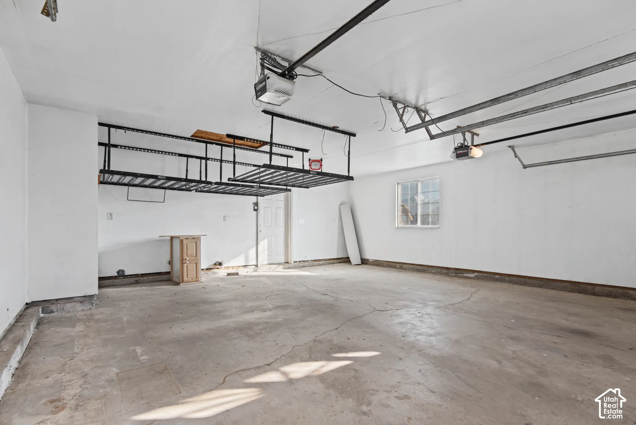 Finished garage interior featuring white-painted walls, overhead storage racks, an automatic garage door opener, and a single-pane window