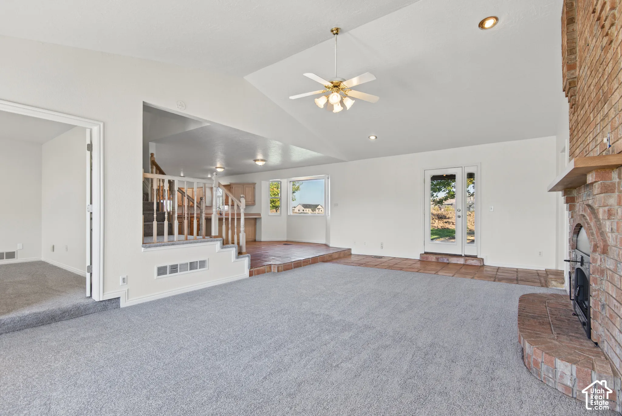 Vaulted ceilings, brick fireplace with a raised hearth, multi-level flooring, wooden stair railings, and glass-paned exterior door