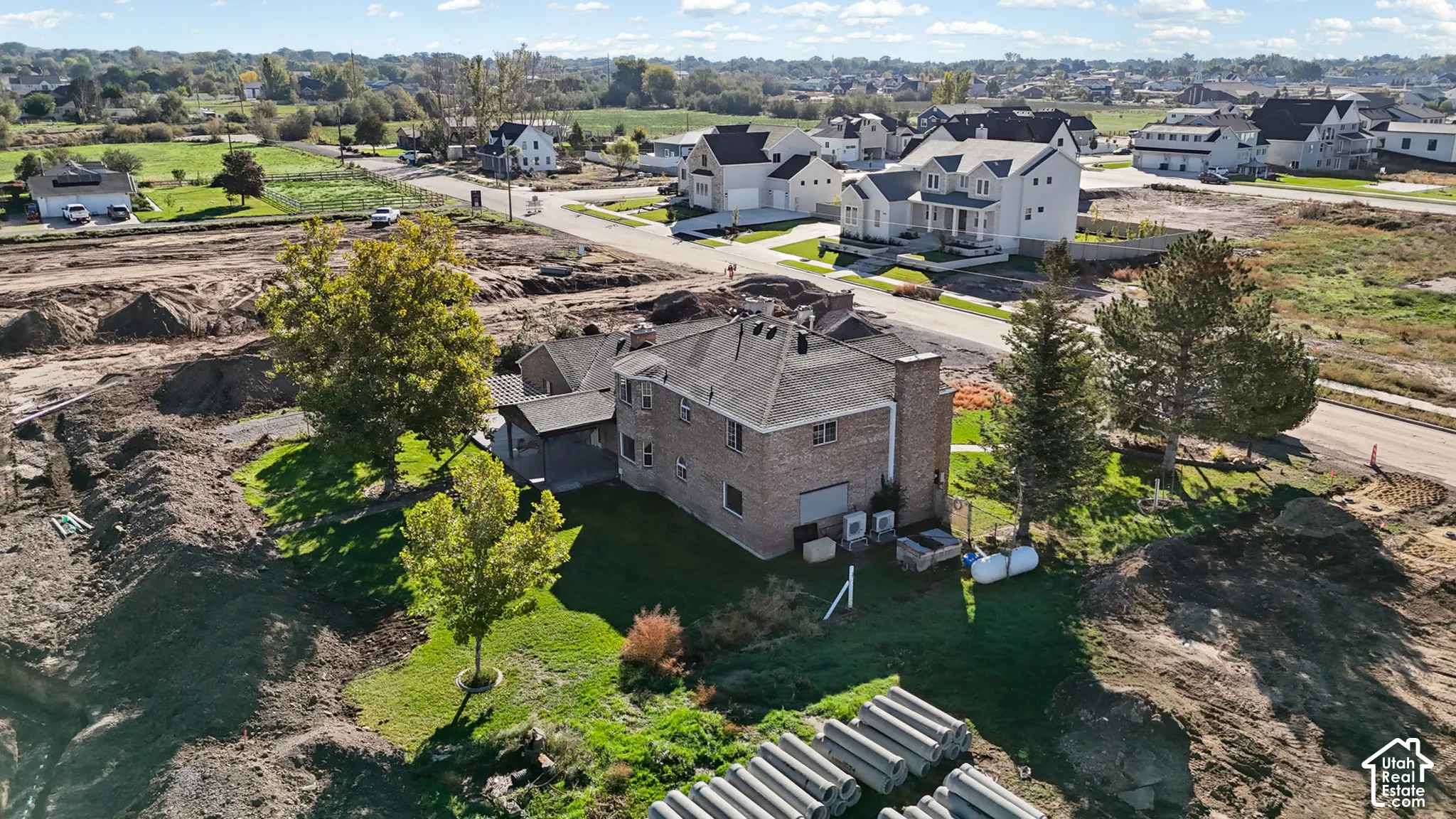 Two-story brick exterior residence featuring a covered patio, mature trees, and a grass-covered lot