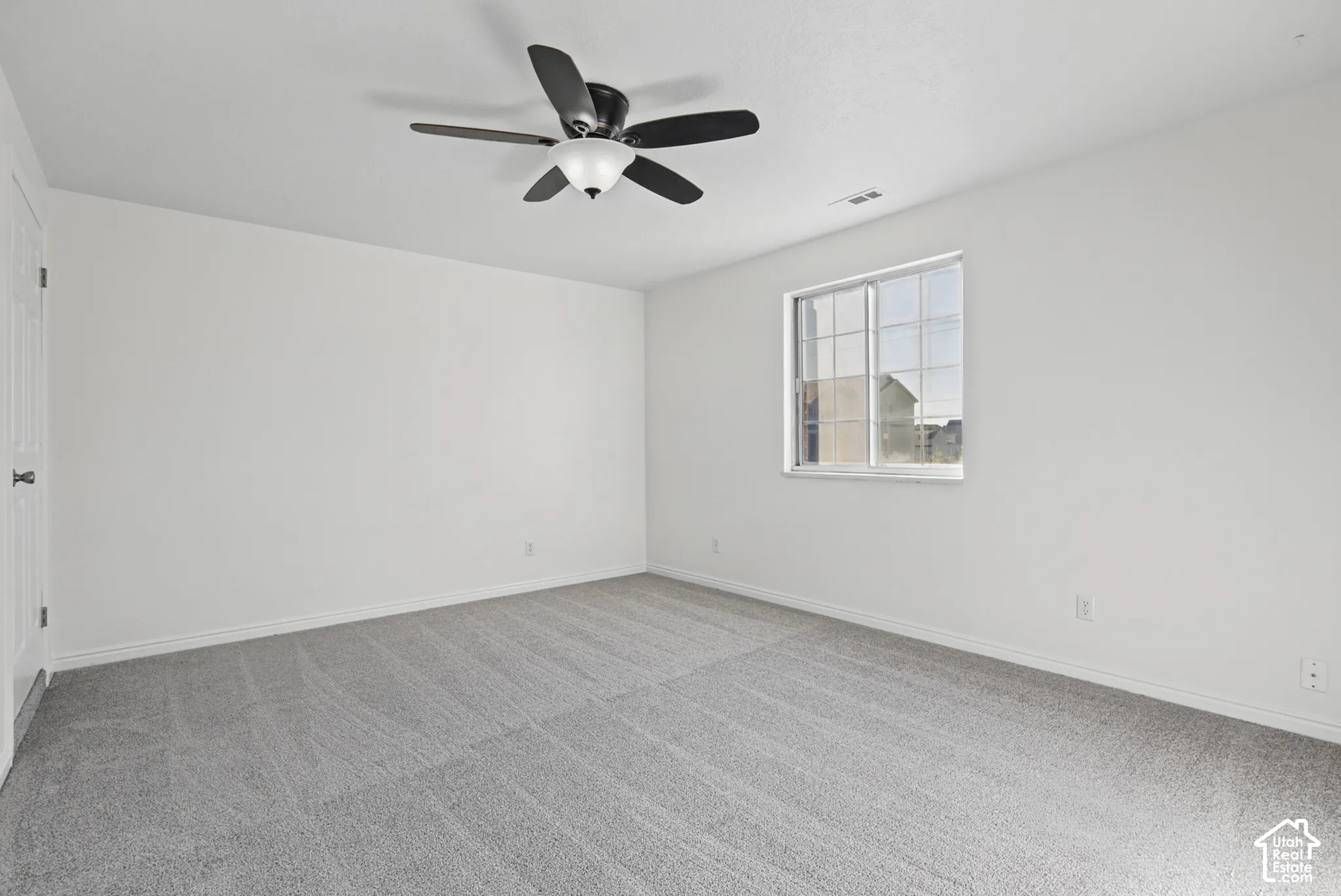 Neutral-toned wall-to-wall carpeting, white interior walls, ceiling fan with integrated lighting, and a multi-pane sliding window