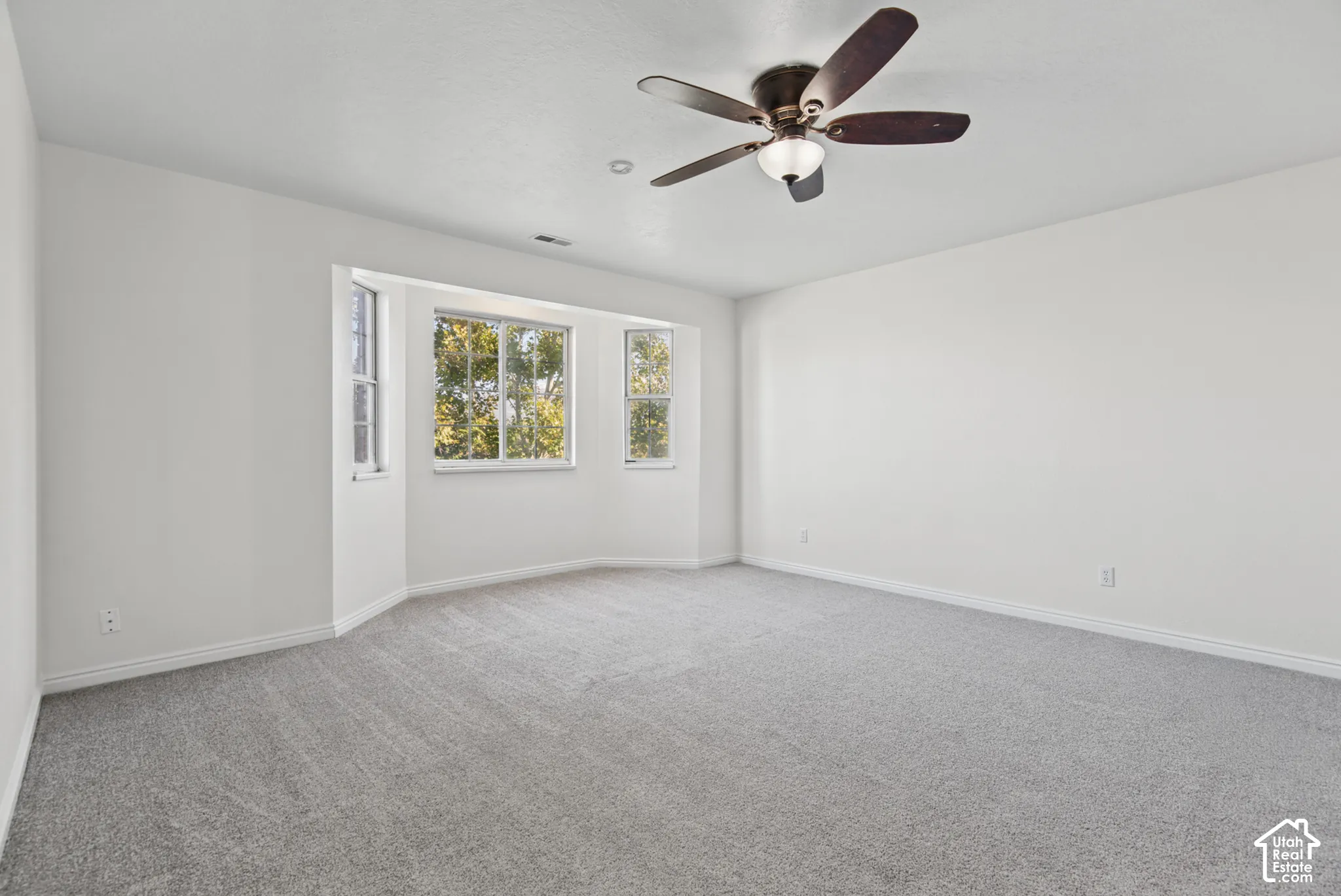 Room featuring neutral wall-to-wall carpeting, a multi-pane bay window, and a ceiling fan with integrated lighting
