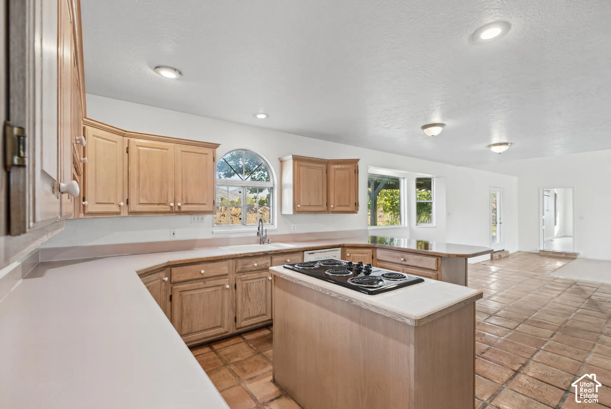 Kitchen featuring wood cabinetry, a central island with a built-in cooktop, tile flooring, recessed lighting, and an arched window