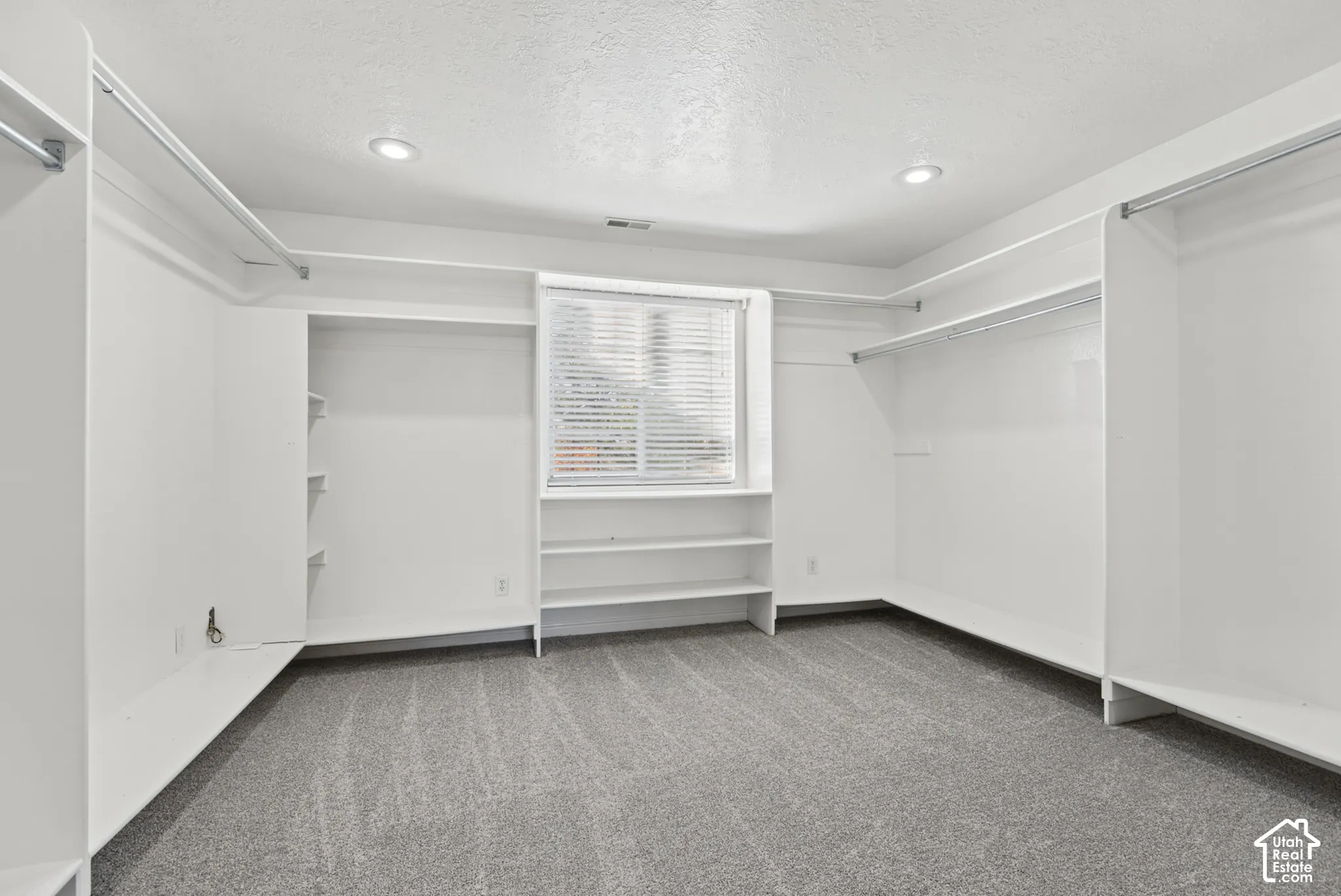 Walk-in closet featuring extensive built-in white shelving, integrated hanging rods, wall-to-wall carpeting, and a window with blinds