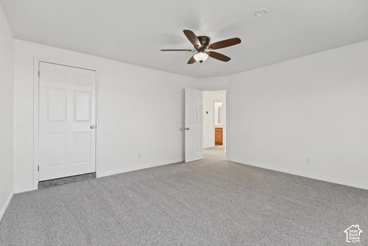 Room featuring neutral wall tones, gray carpeting, a multi-blade ceiling fan with integrated lighting, and white paneled doors