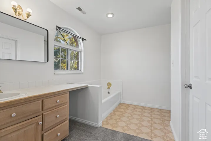 Bathroom featuring wood-finish cabinetry, arched window with decorative grille, built-in bathtub with tiled surround, and integrated vanity countertop