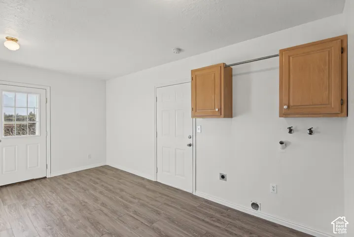 Laundry room featuring wood-finish flooring, two wall-mounted wood cabinetry units, a stainless steel clothing rod, and exterior access via a glass-paneled door