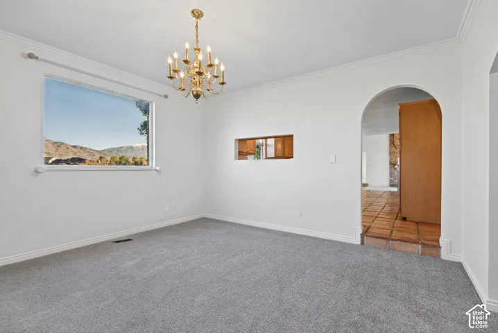 Interior space featuring a vaulted ceiling with crown molding, a multi-light brass chandelier, and a large picture window showcasing mountain scenery