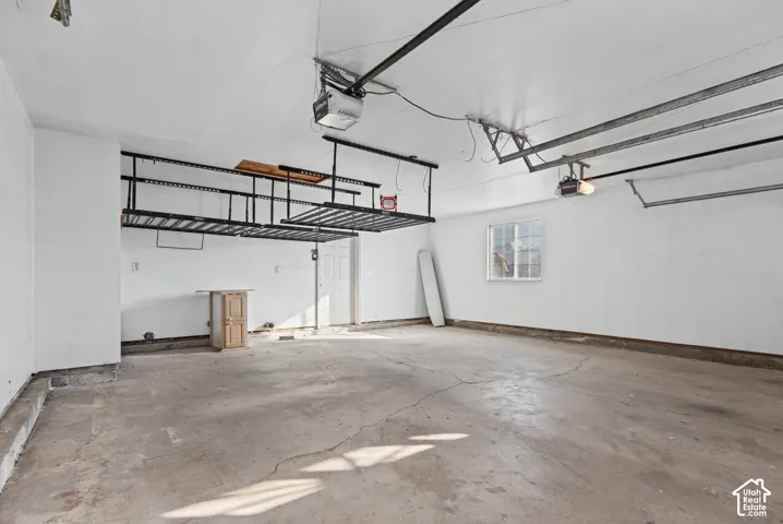Finished garage interior featuring white-painted walls, overhead storage racks, an automatic garage door opener, and a single-pane window