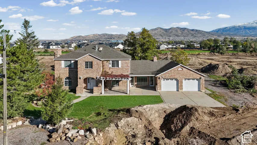 Two-story brick exterior featuring a pergola, concrete driveway, attached two-car garage, and mountain backdrop