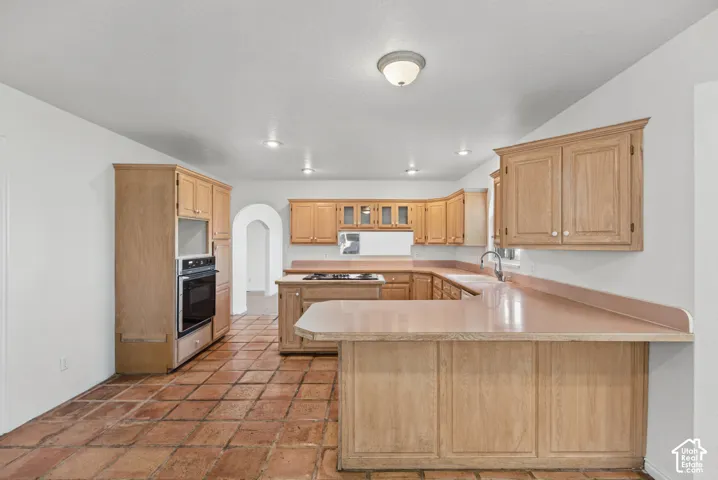Kitchen featuring natural wood cabinetry, a peninsula breakfast bar with extended countertop, an integrated wall oven, and tile flooring