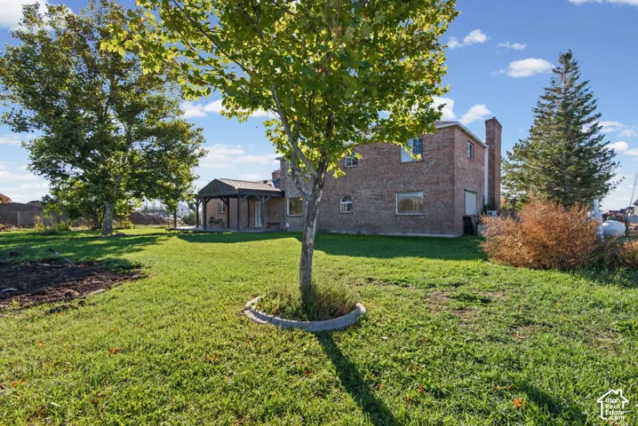 Brick exterior home featuring a covered patio, stone chimney, and mature trees on a sprawling grass lot