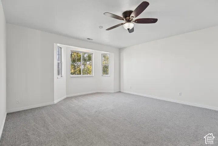 Room featuring neutral wall-to-wall carpeting, a multi-pane bay window, and a ceiling fan with integrated lighting