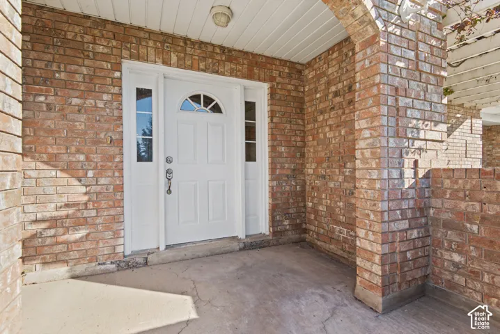Covered entryway featuring a red brick exterior, a white front door with a decorative arched window, sidelight windows, and a built-in overhead light fixture