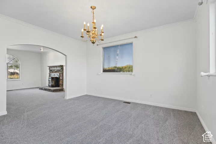 Interior space featuring a traditional metal chandelier, arched entryway, stone-faced fireplace with a metal insert, neutral carpeting, and crown molding