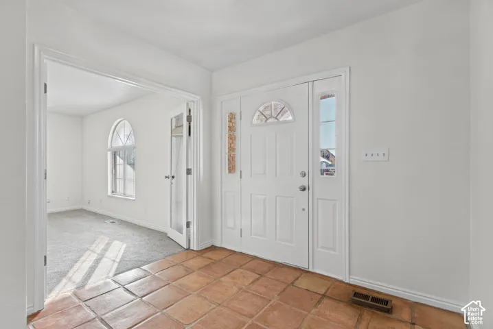 Entryway featuring terra cotta tile flooring, a paneled front door with decorative glass inlay, and sidelight windows