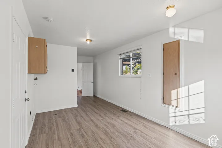 Interior space featuring wood-finish flooring, a single-pane window with a roller shade, recessed wall storage with a wood-finish door, wall-mounted upper cabinetry, and ceiling-mounted dome lighting