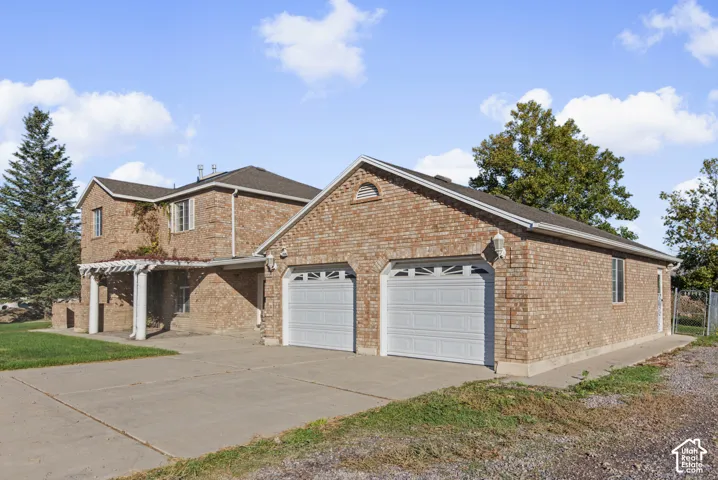 Two-story brick exterior featuring a built-in pergola, dual-car garage with arched decorative windows, and a paved concrete driveway