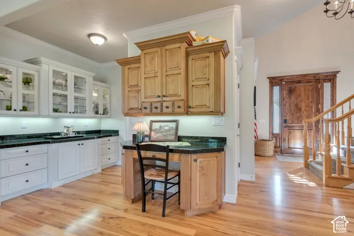 Custom cabinetry with wood-finish upper and lower storage, stone-surfaced countertops, built-in desk workstation, wood-finish flooring, and crown molding