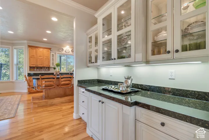 Custom cabinetry with glass-fronted upper doors, under-cabinet lighting, dark stone countertops, and wood-finish flooring