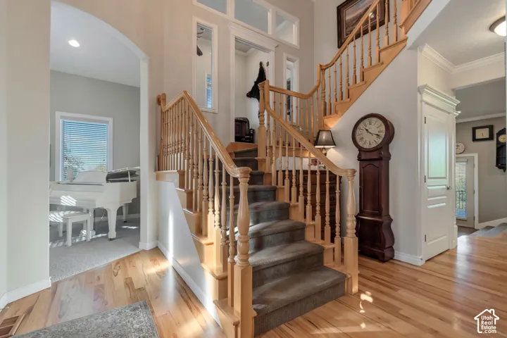 Foyer featuring wood-finish flooring, a staircase with a wooden handrail and balusters, arched architectural entryways, and transom windows