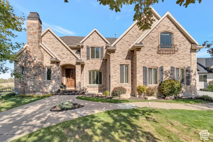 Two-story brick exterior featuring a multi-gabled roofline, stone chimney, arched recessed entryway, and decorative window shutters