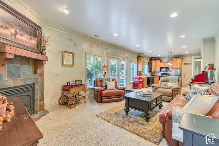 Fireplace with stone-tile surround and prominent timber mantel, recessed lighting, crown molding, glass-paned doors, and natural wood cabinetry