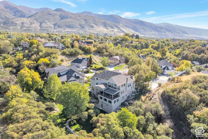 Aerial perspective featuring a multi-level residence with a tiered deck, mountain backdrop, and surrounding mature woodland foliage