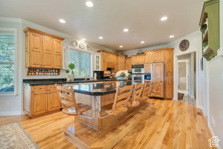 Kitchen featuring honey-toned wood cabinetry, stone countertops, a raised central island with built-in seating, wood-finish flooring, and integrated double wall ovens