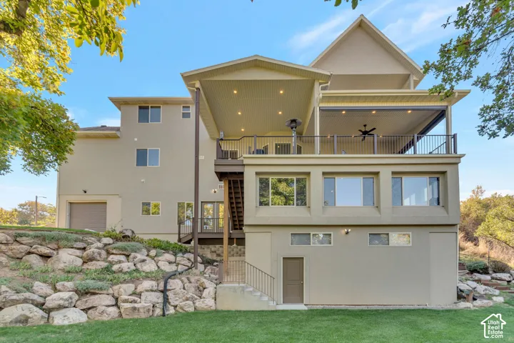 Multi-level exterior featuring a covered deck with recessed lighting, black metal railing, stacked boulder retaining walls, and a lower-level yard