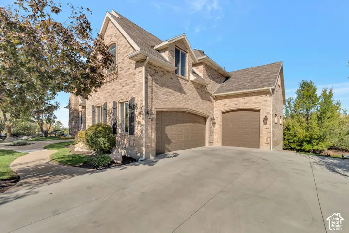 Multi-story brick exterior featuring a three-car garage, steep roof pitches with dual gables, concrete driveway, and arched garage door openings