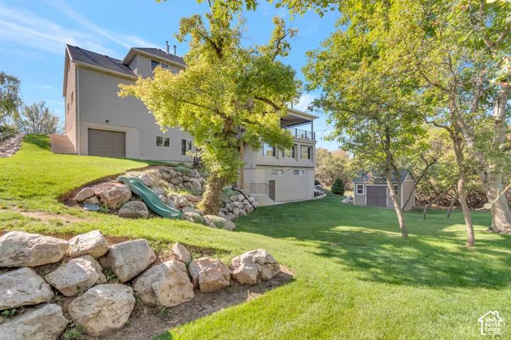 Multi-level exterior featuring a stone retaining wall, detached storage shed, attached garage, and elevated deck