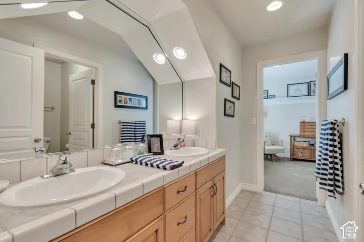 Jack and Jill Bathroom.  Dual-sink vanity with tile countertop, undermount basins, wood cabinetry, and full-width beveled mirror