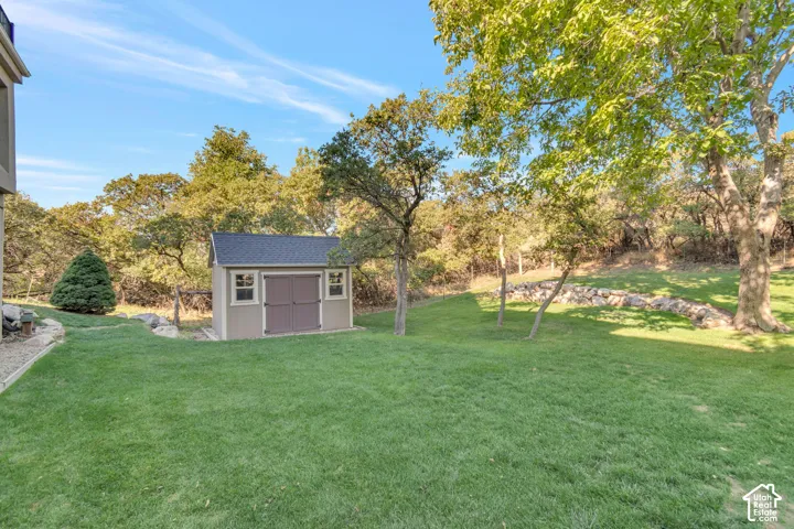 Backyard featuring a manicured lawn, mature trees, a detached storage shed with double doors, and natural stone hardscaping