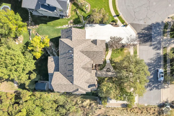 Aerial perspective of a multi-gabled architectural roofline, concrete driveway, stone-accented landscaping, and mature perimeter trees situated on a cul-de-sac lot