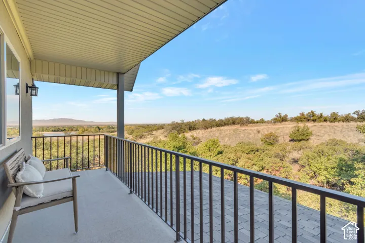 Covered balcony featuring metal railings, textured concrete flooring, wall-mounted light fixture, and mountainous landscape