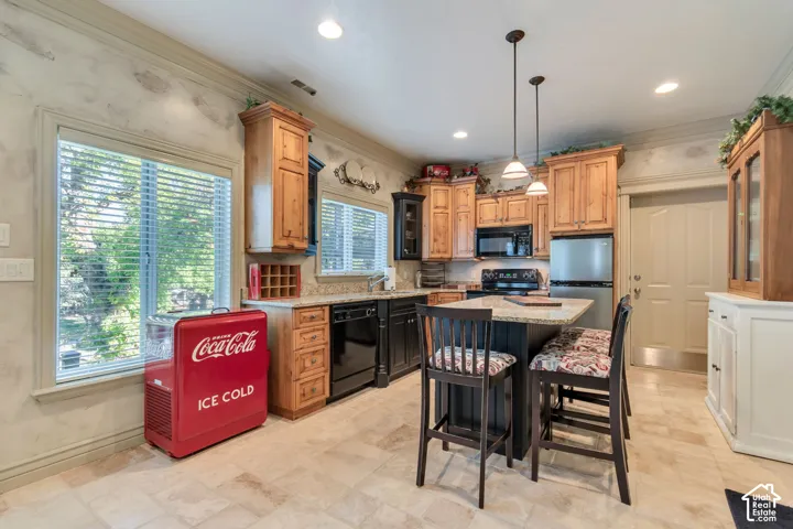 Kitchen featuring natural wood cabinetry, stone-finish countertops, a central island with a contrasting dark base, tile flooring, and dual pendant lighting