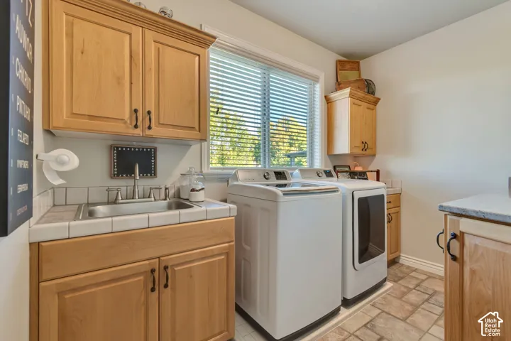 Natural wood cabinetry, tiled countertop with integrated drop-in sink, stone-finish tile flooring, and dedicated laundry hookups