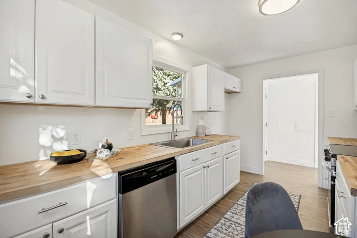 Kitchen featuring white Shaker-style cabinetry, wood-surface countertops, stainless steel undermount sink with arched faucet, stainless steel dishwasher, and wood-finish flooring