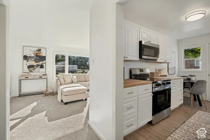 Kitchen featuring white shaker-style cabinetry, wood-surface countertops, and stainless steel appliances, including a microwave and range