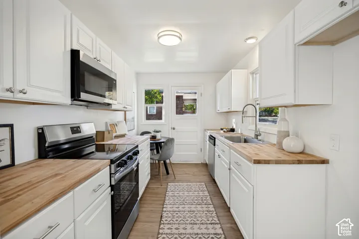 Kitchen featuring white shaker-style cabinetry, wood-surface countertops, stainless steel appliances, a high-arc faucet, and wood-finish flooring