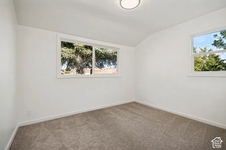 Neutral-toned carpeting, vaulted ceilings, and dual sliding and single-hung windows featuring exterior greenery