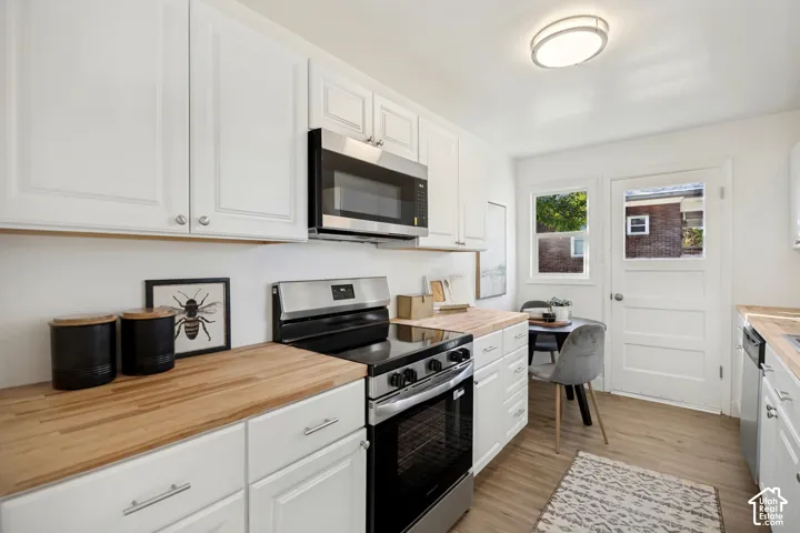Kitchen featuring white shaker-style cabinetry, wood-finish countertops, stainless steel appliances, and wood-finish flooring