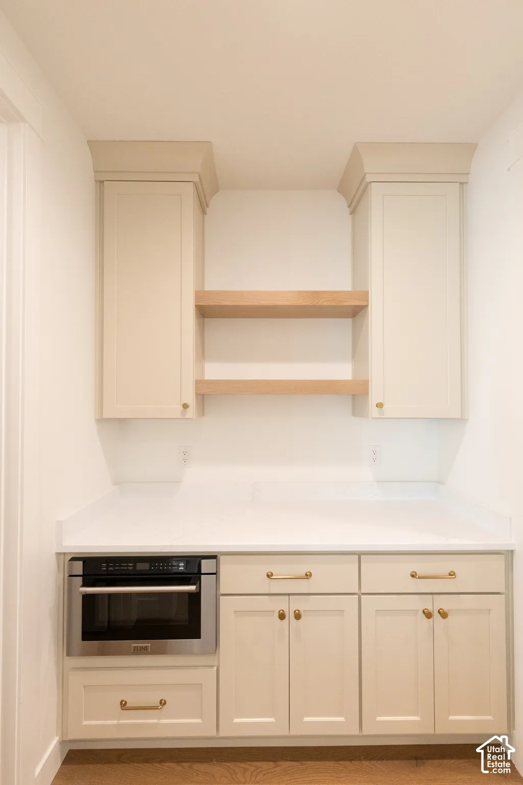 Custom cabinetry featuring recessed-panel doors, solid surface countertops, integrated microwave, open wood shelving, and metallic hardware