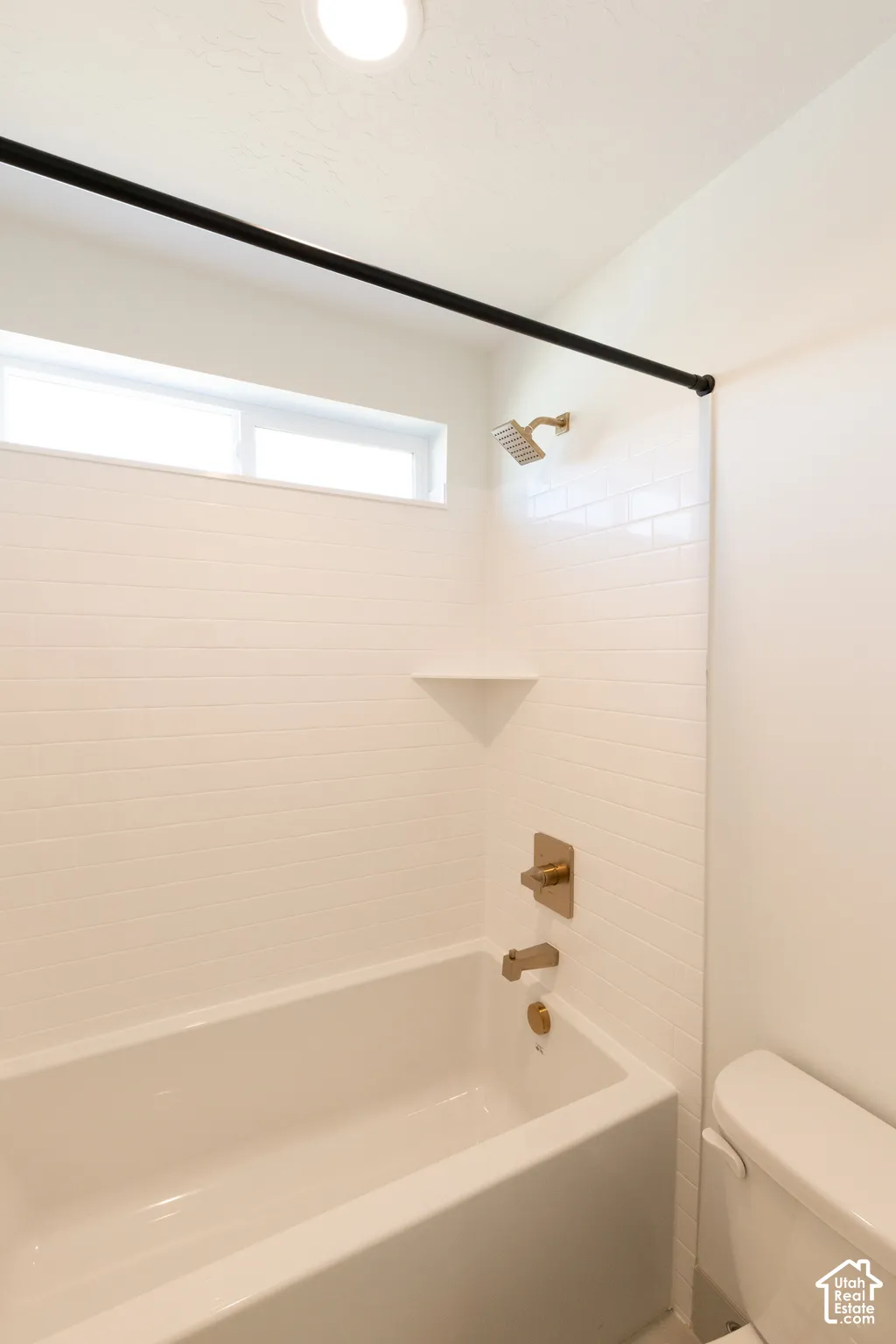 Bathtub and shower surround featuring white subway tile, a built-in corner shelf, rectangular matte metallic hardware, and a horizontal transom window