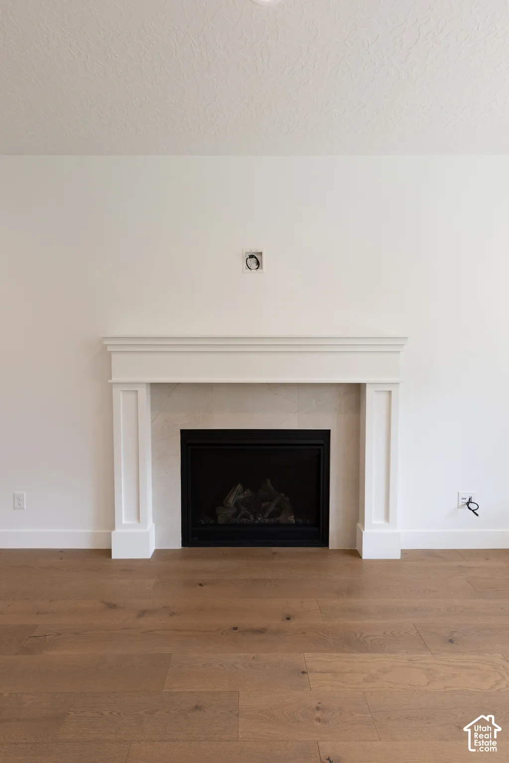 Fireplace featuring a white mantel, stone-tile surround, black metal firebox, and wood-finish flooring