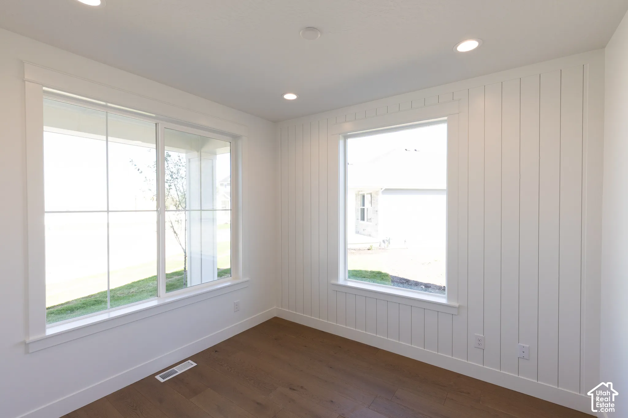 Room featuring vertical board-and-batten wall paneling, wood-finish flooring, recessed lighting, and large windows with integrated grids