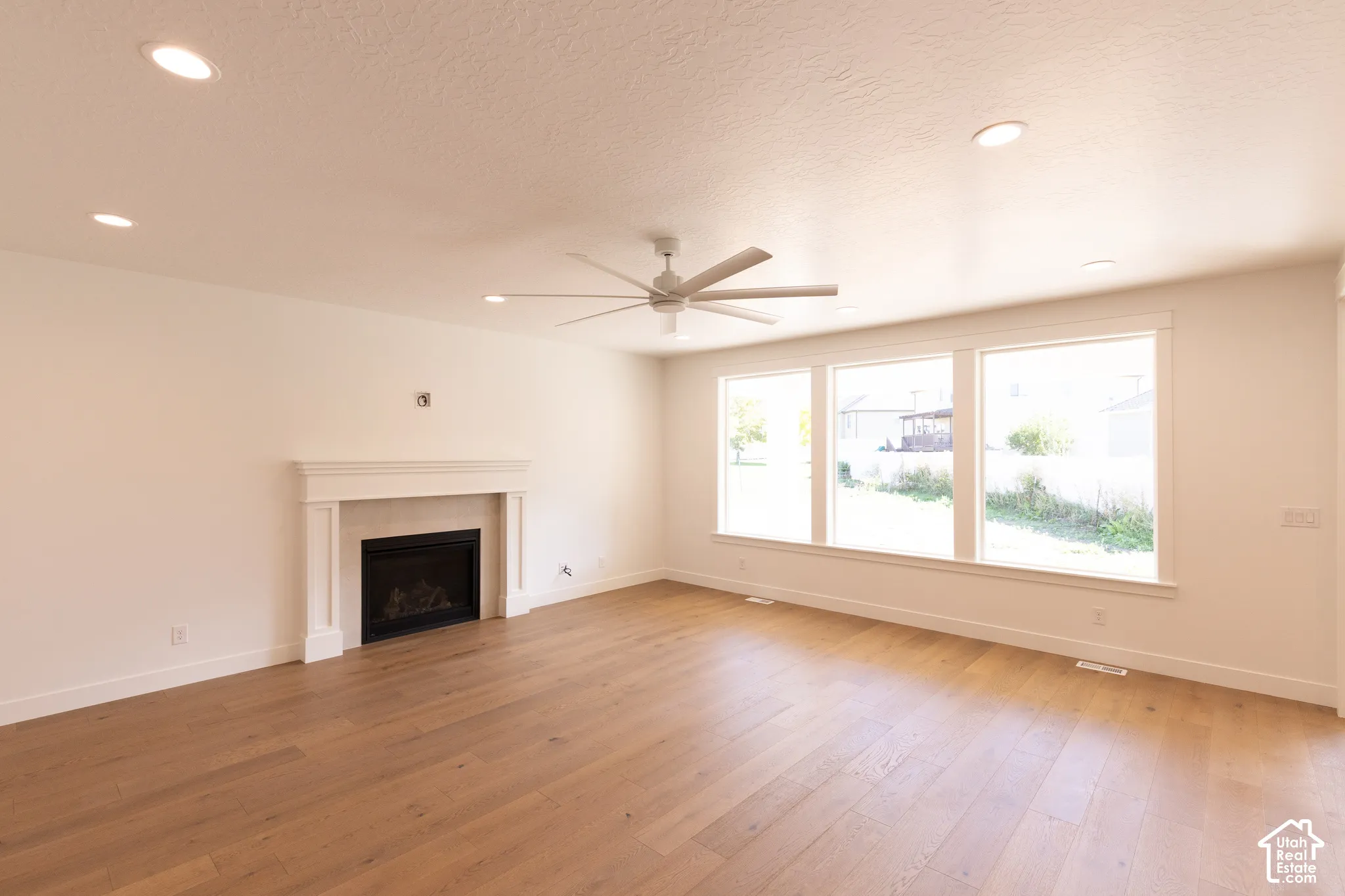 Living space featuring wood-finish flooring, a fireplace with a white mantel, recessed lighting, and a ceiling fan